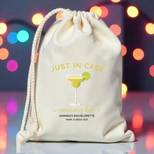 May include: A white drawstring bag with the text "JUST IN CASE" and a margarita glass with a lime wedge. The bag also has the text "recovery kit" and "AMANDA'S BACHELORETTE MIAMI, FLORIDA 2025".