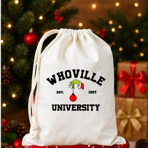 May include: A white drawstring bag with the text "WHOVILLE UNIVERSITY" in black. The design includes a green hand holding a red ornament. The bag is set against a backdrop of Christmas trees and wrapped gifts.