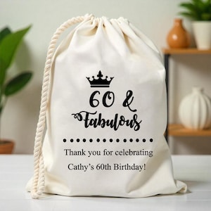 May include: White cotton drawstring bag with black text that reads "60 & Fabulous" with a crown above the text. The bag also has the text "Thank you for celebrating Cathy's 60th Birthday!"