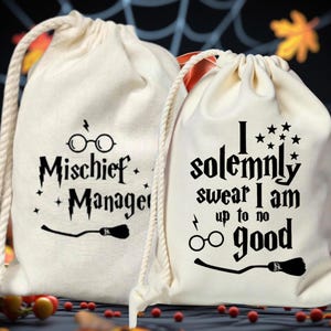 以下が含まれることがあります： 黒い文字とグラフィックが入った、2つのクリーム色の巾着袋。1つのバッグには、メガネとほうきで「Mischief Managed」と書かれています。もう1つは、星、メガネ、稲妻、ほうきで「I solemnly swear I am up to no good」と書かれています。