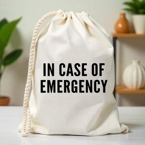 May include: A white canvas drawstring bag with the text "IN CASE OF EMERGENCY" printed in black.