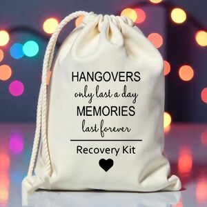K&ouml;nnte beinhalten: Ein wei&szlig;er Kordelzugbeutel mit dem Text "HANGOVERS only last a day MEMORIES last forever Recovery Kit" und einem schwarzen Herzen.