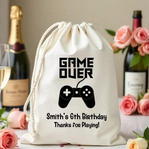 May include: White drawstring bag with black text that reads "GAME OVER" and a black video game controller graphic. The bag also has the text "Smith's 6th Birthday Thanks for Playing!"