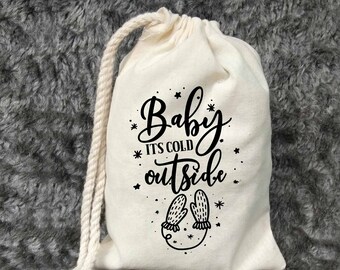 Könnte beinhalten: Eine weiße Baumwolltasche mit Kordelzug, mit schwarzem Text, der "Baby it's cold outside" lautet, und einer schwarzen Illustration von Fäustlingen.