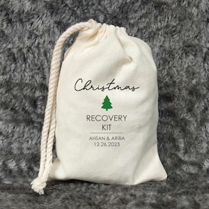 May include: A white cotton drawstring bag with the text "Christmas Recovery Kit" and a green Christmas tree graphic. The bag also includes the names "Ahsan & Ariba" and the date "12.26.2023".