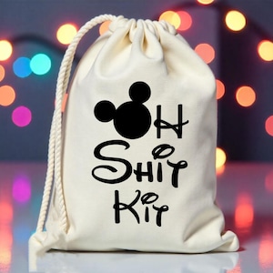 Op de afbeelding: Crème kleurige trekkoordtas met een zwarte Mickey Mouse hoofd silhouette en de woorden "H Shit Kit" in een speels lettertype. De tas heeft een wit touwtrekkoord en staat tegen een vage achtergrond van kleurrijke lichten.