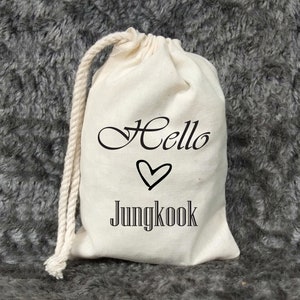Peut inclure: Un sac en toile blanc avec le texte "Hello" en écriture cursive, un symbole de cœur et le texte "Jungkook" imprimé dessus.