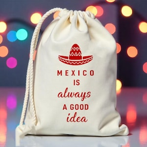 May include: Off-white drawstring bag with a red sombrero graphic and the text "MEXICO IS always A GOOD idea". The bag has a white rope drawstring closure and is set against a blurred background of colorful lights.