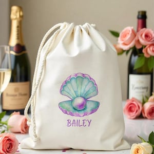Puede incluir: Una bolsa de tela blanca con un diseño de concha de mar púrpura y verde y una perla en su interior. La bolsa tiene el nombre "BAILEY" impreso en letras moradas.