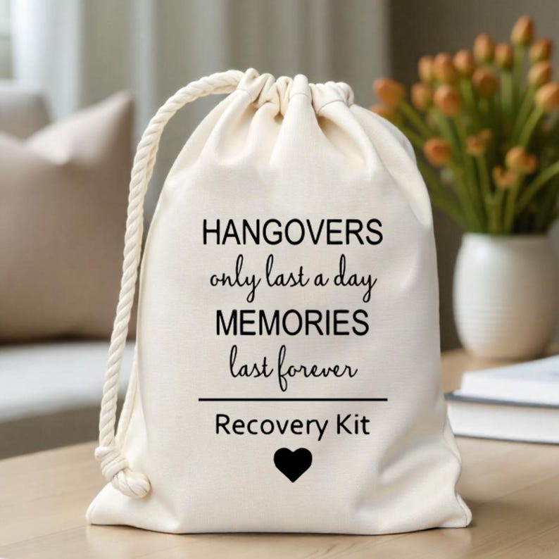 K&ouml;nnte beinhalten: Eine wei&szlig;e Baumwoll-Kordeltasche mit dem Text "Hangovers only last a day MEMORIES last forever Recovery Kit" und einem schwarzen Herzen.