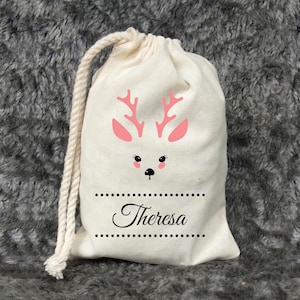 May include: A white cotton drawstring bag with a pink reindeer design and the name "Theresa" printed in black.