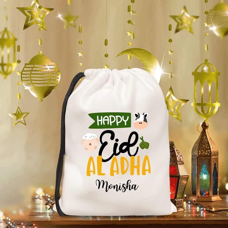 May include: White drawstring bag with a green and yellow design that says 'Happy Eid Al Adha Monisha' with a cow and sheep illustration.