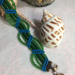 May include: A green and blue beaded bracelet with a brass clasp and a Chinese coin charm. The bracelet is made with small, round beads and has a woven design.