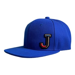Peut inclure: Une casquette de baseball bleu royal avec une grande lettre "J" en feutre multicolore sur le devant.