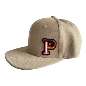 Könnte beinhalten: Beige Baseballkappe mit flachem Schirm. Die Kappe hat einen aufgenähten Aufnäher mit dem Buchstaben "P" in Rot, Schwarz und Gelb. Der Hut ist aus strapazierfähigem Stoff gefertigt und hat eine strukturierte Krone.