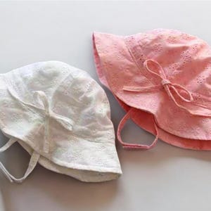 Puede incluir: Dos sombreros de sol bordados, uno blanco y otro rosa. Ambos sombreros tienen ala ancha, un lazo y correas para la barbilla. Los sombreros est&aacute;n hechos de tela ligera, ideal para la protecci&oacute;n solar.
