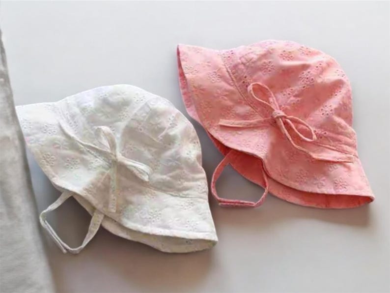 Puede incluir: Dos sombreros de sol bordados, uno blanco y otro rosa. Ambos sombreros tienen ala ancha, un lazo y correas para la barbilla. Los sombreros est&aacute;n hechos de tela ligera, ideal para la protecci&oacute;n solar.
