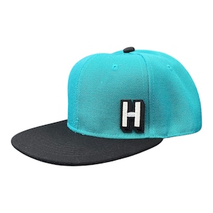 Peut inclure: Casquette de baseball turquoise et noire avec une visière plate. Le chapeau comporte un écusson blanc et noir avec la lettre "H" à l'avant. Le bouton supérieur est noir.