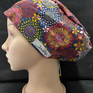 May include: A blue scrub cap with a colourful floral pattern and a white label that says "ScrubLife".