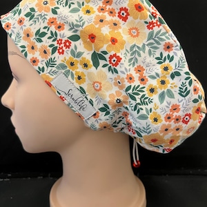 May include: A scrub cap with a floral pattern in yellow, orange, and red on a white background, with green leaves. The cap includes a drawstring and a label that says "Scrublife".