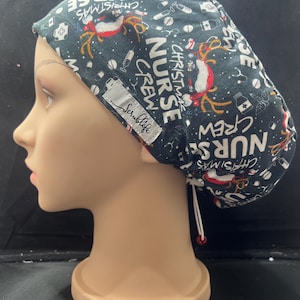 May include: A dark blue scrub cap with a Christmas theme, featuring reindeer, medical symbols, and the text "Christmas Nurse Crew." The cap has a white drawstring and a small tag that says "Scrublife."