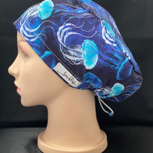 May include: A blue and white patterned surgical scrub hat with a drawstring closure. The hat features a print of jellyfish and the text "ScrubLife".