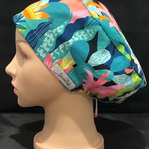 Peut inclure: Un bonnet chirurgical bleu, vert, rose et jaune à motifs avec une étiquette blanche indiquant "ScrubLife".