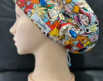 May include: A blue and white scrub hat with a colorful cartoon print featuring characters from popular animated television shows. The hat has a drawstring and a label that reads "Scrublife".