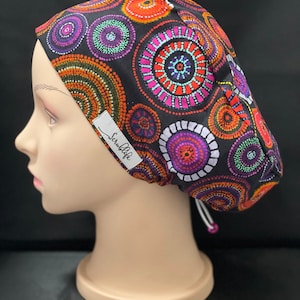 May include: A black scrub cap with a colourful circular pattern. The cap has a white drawstring and a white label that says "ScrubLife".