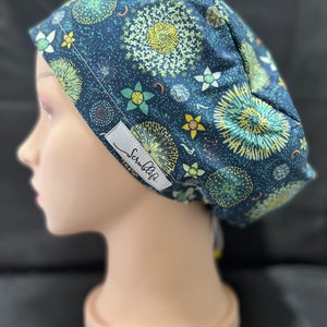 May include: A blue scrub cap with a white and yellow floral pattern. The cap has a tie on the back and the text "ScrubLife" is printed on the side.