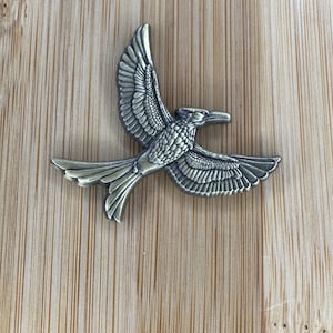 May include: A gold-toned metal bird pendant with intricate details. The bird is in flight with its wings spread wide. The pendant is a decorative piece with a vintage aesthetic.