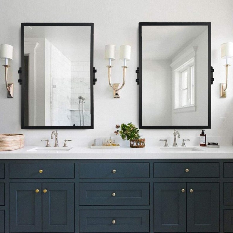 May include: A bathroom vanity with two sinks and a white countertop. The vanity has three drawers on each side and two cabinets with gold knobs. Two black framed mirrors hang above the sinks. Each mirror has two gold wall sconces with white shades.