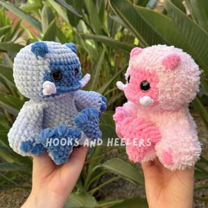May include: Two crocheted plush toys, one blue and one pink, with white accents. The toys have large eyes and are shaped like a cartoon animal.