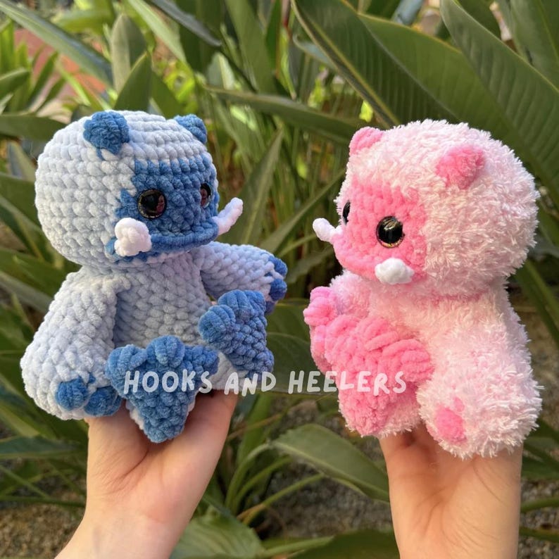 May include: Two crocheted plush toys, one blue and one pink, with white accents. The toys have large eyes and are shaped like a cartoon animal.
