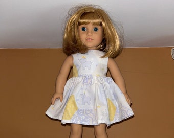 Könnte beinhalten: Eine Puppe, die ein weißes Kleid mit gelben und blauen Akzenten und einem Muster von Elefanten mit Kronen trägt. Das Kleid hat eine geraffte Taille und einen vollen Rock.
