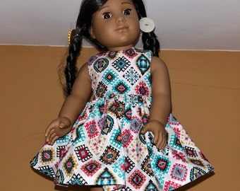 Könnte beinhalten: Eine braungefärbte Puppe mit schwarzen Zöpfen, die ein weißes Kleid mit einem bunten geometrischen Muster trägt. Das Kleid ist ärmellos und hat einen gerafften Rock.