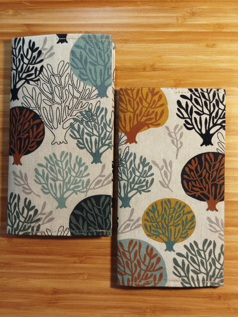 May include: Two rectangular fabric covers featuring a repeating pattern of stylized trees in shades of teal, mustard yellow, dark brown, and black on an off-white background. The covers have visible stitched edges and a textured woven appearance.