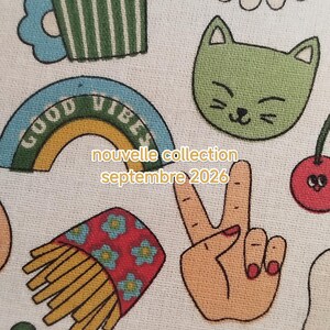 May include: A white fabric featuring a repeating pattern of colorful embroidered icons including a green cat face, a rainbow with the text GOOD VIBES, a carton of french fries, a peace sign hand, and a daisy. Text reads nouvelle collection septembre 2026.