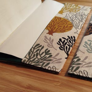 May include: A fabric notebook cover featuring a cream-colored background with a repeating pattern of stylized coral and seaweed shapes in shades of mustard yellow, dark green, sage green, and black, shown partially open with white paper pages.