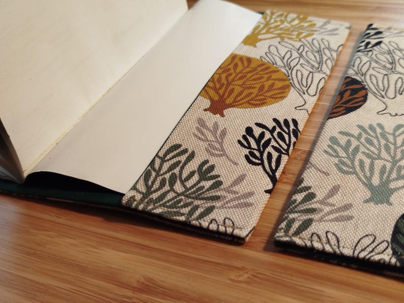 May include: A fabric notebook cover featuring a cream-colored background with a repeating pattern of stylized coral and seaweed shapes in shades of mustard yellow, dark green, sage green, and black, shown partially open with white paper pages.
