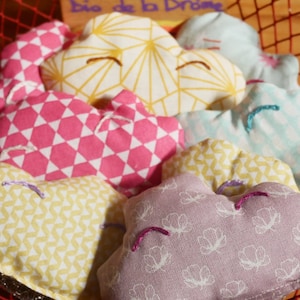 Può includere: Cinque cuscini in tessuto a forma di nuvola in un cesto. I cuscini sono di vari colori e motivi, tra cui giallo, rosa, blu e viola.