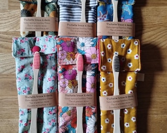May include: Six bamboo toothbrushes with colored bristles, each housed in a patterned fabric sleeve. Each sleeve features a paper band labeled 'Pochette brosse à dents' and includes a snap closure. The patterns include floral, striped, and geometric designs.