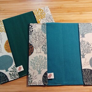 May include: Two rectangular fabric book covers featuring a solid teal or dark green center panel flanked by side panels with a cream background and a repeating pattern of stylized trees in shades of blue, mustard yellow, and dark gray.