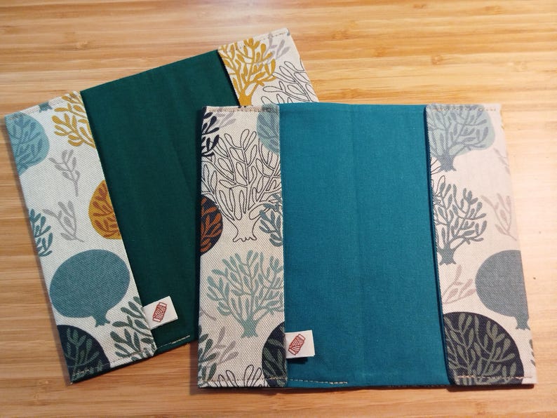 May include: Two rectangular fabric book covers featuring a solid teal or dark green center panel flanked by side panels with a cream background and a repeating pattern of stylized trees in shades of blue, mustard yellow, and dark gray.