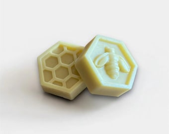 May include: Two hexagonal, pale yellow wax melts. One features a honeycomb pattern, and the other has a raised bee design. The melts are likely scented and designed for use in a wax warmer, adding fragrance to a room.