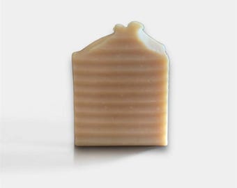 May include: A light brown, rectangular bar of handmade soap with a ridged surface. The top of the soap has an irregular shape. The soap is likely unscented and suitable for sensitive skin. The soap's dimensions are approximately 8 cm x 5 cm.