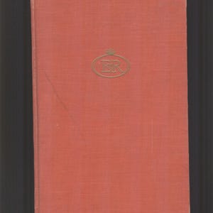 May include: A vintage book with a textured, reddish-orange cover. The cover features a gold-colored emblem in the upper right corner. The book's spine is on the left side, and the background is dark.