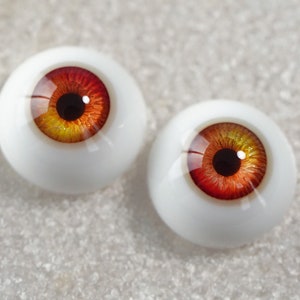 May include: Two realistic-looking glass doll eyes with a white sclera, a black pupil, and a red and yellow iris.