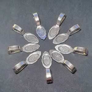 May include: Ten silver-toned pendant bails with a decorative, textured oval design. The bails are arranged in a circle on a grey surface.