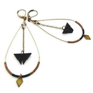Puede incluir: Un par de pendientes de tono dorado con abalorios de mariposa de madera negra y detalles en forma de diamante dorado. Los pendientes están hechos con una combinación de cadena, alambre y cuentas.